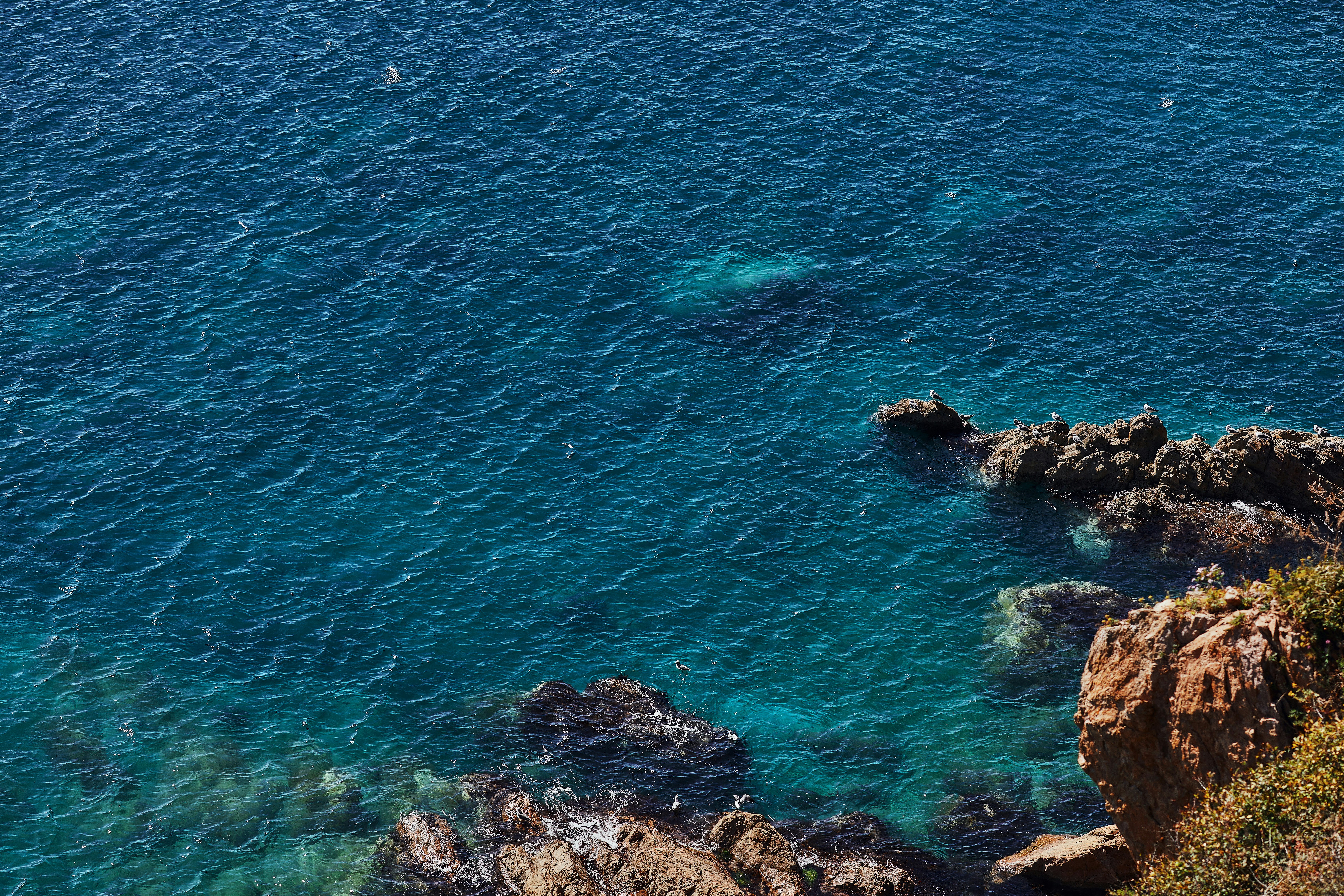 brown rocky mountain beside blue sea during daytime